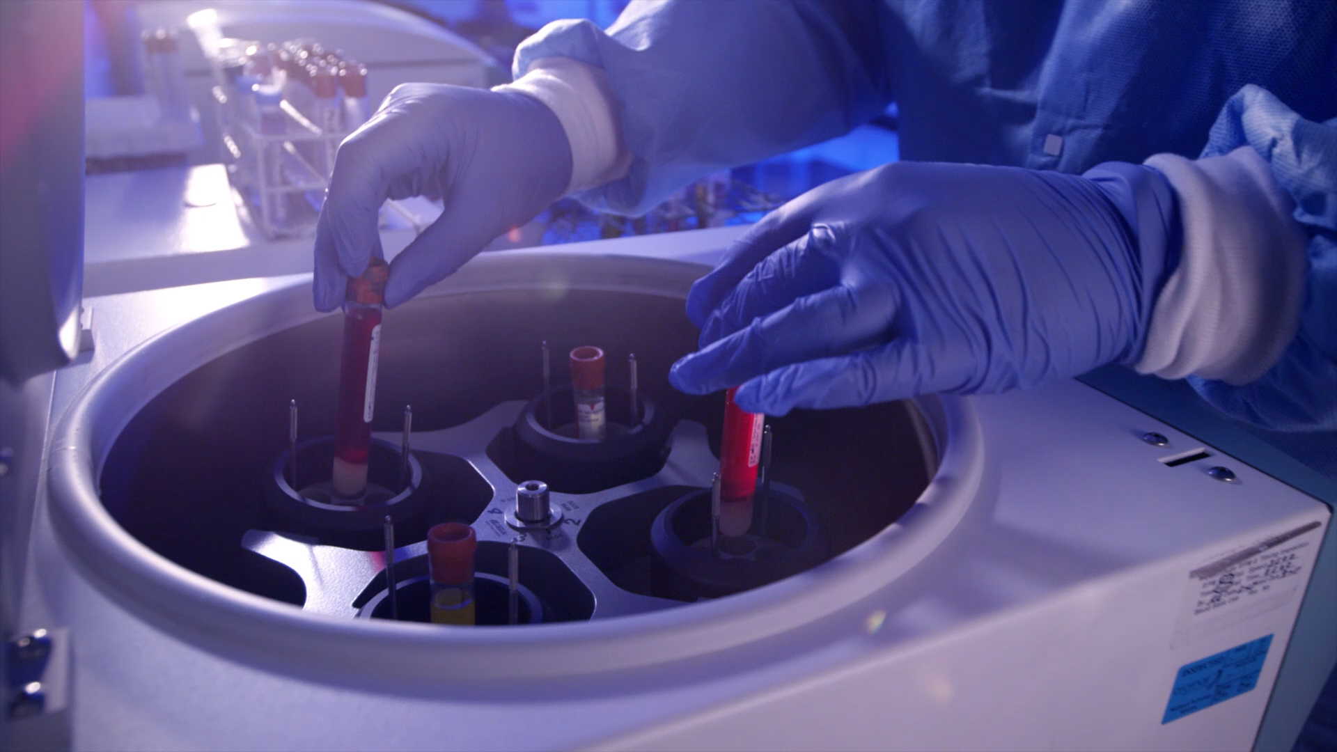 Gloved lab technician places blood sample tubes into a centrifuge inside a hospital laboratory.