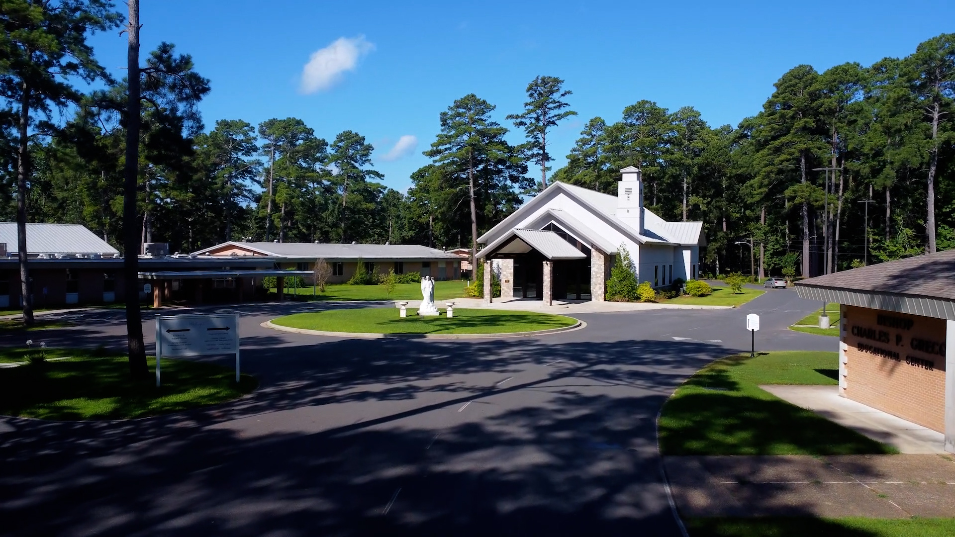 Aerial drone shot of the Holy Angels campus, including the chapel, educational center, and surrounding grounds framed by tall pine trees.