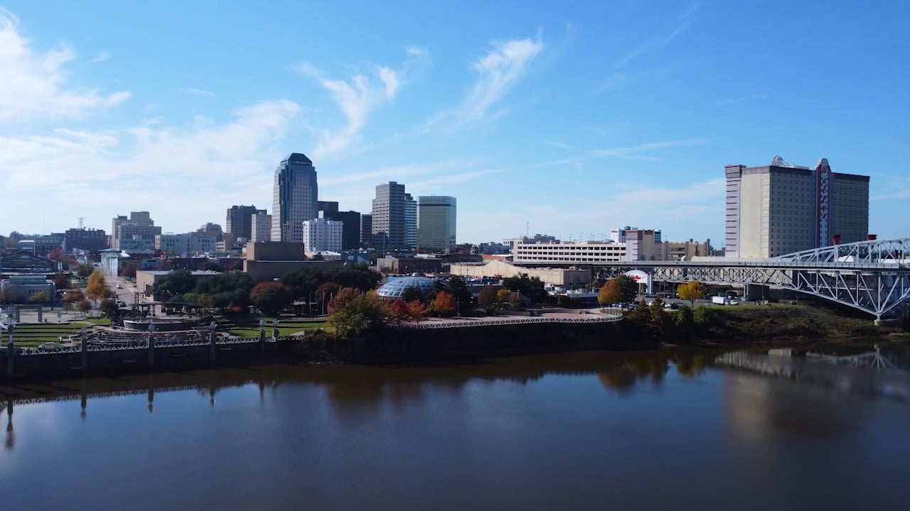 Aerial view of the Downtown Shreveport skyline across the Red River, framed by the Texas Street Bridge and autumn foliage along the riverbank.