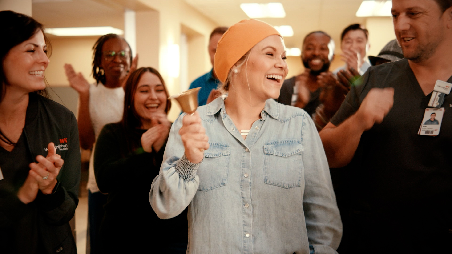 Cancer patient in an orange head wrap rings the end-of-treatment bell while her Willis-Knighton care team cheers and applauds around her.